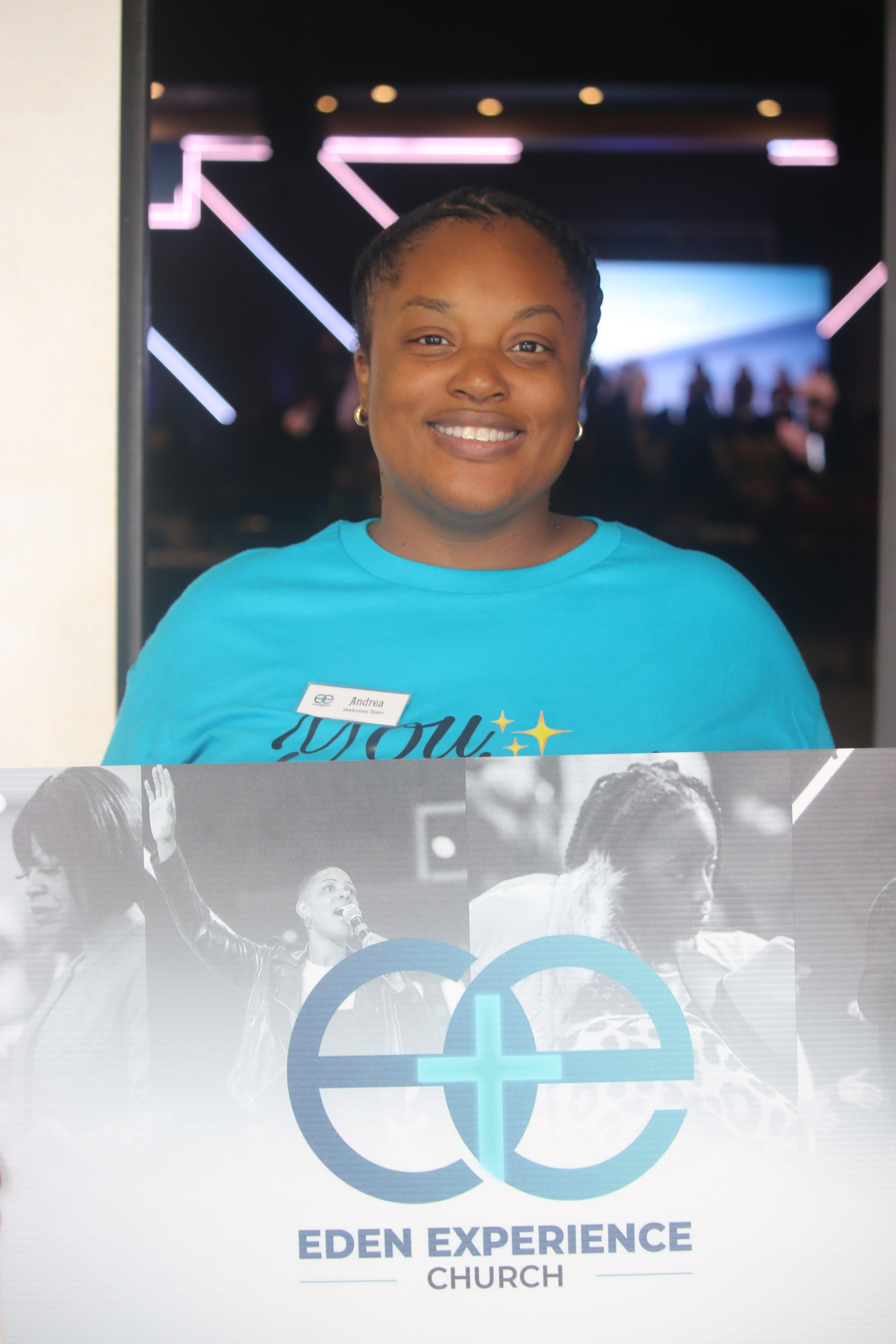 Eden welcome team member in blue holding an Eden Experience sign